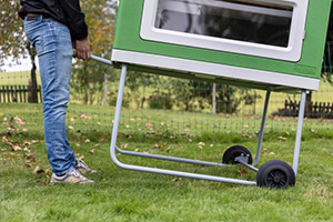 Seitenansicht vom mobilen Hühnerstall Mobile Coop mit stabilem Metallgestell mit zwei Rädern und Griff an der Seite